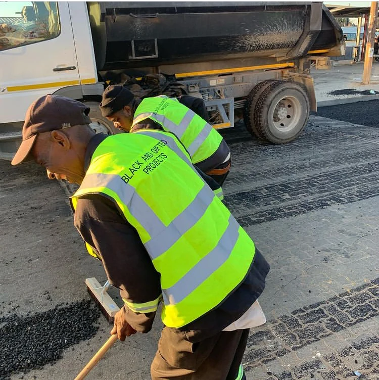 BG Projects crew in branded high-visibility workwear laying asphalt beside a tipper truck